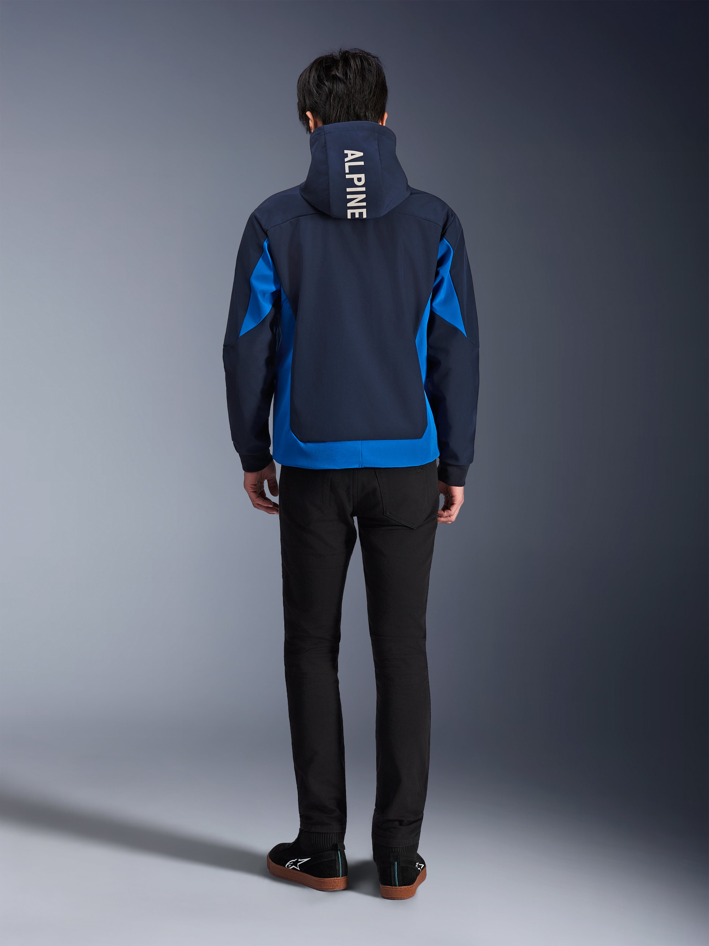 Alpinestars Radium Tech Hoodie, Night Navy und Royal Blue, Rückansicht mit vertikalem 'ALPINE'-Branding auf der Kapuze, königsblauen Seiteneinsätzen und Saum, lässiger urbaner Motorrad-Hoodie mit winddichtem 3L-Shell, getragen mit schwarzer Hose