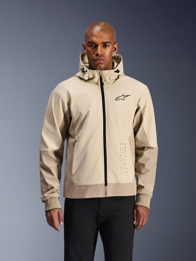 Alpinestars Radium Tech Hoodie in Mastic Aluminum, light beige and tan urban motorcycle jacket, black front zipper and small chest logo, modeled by a man in black pants, technical windproof shell with contemporary streetwear styling