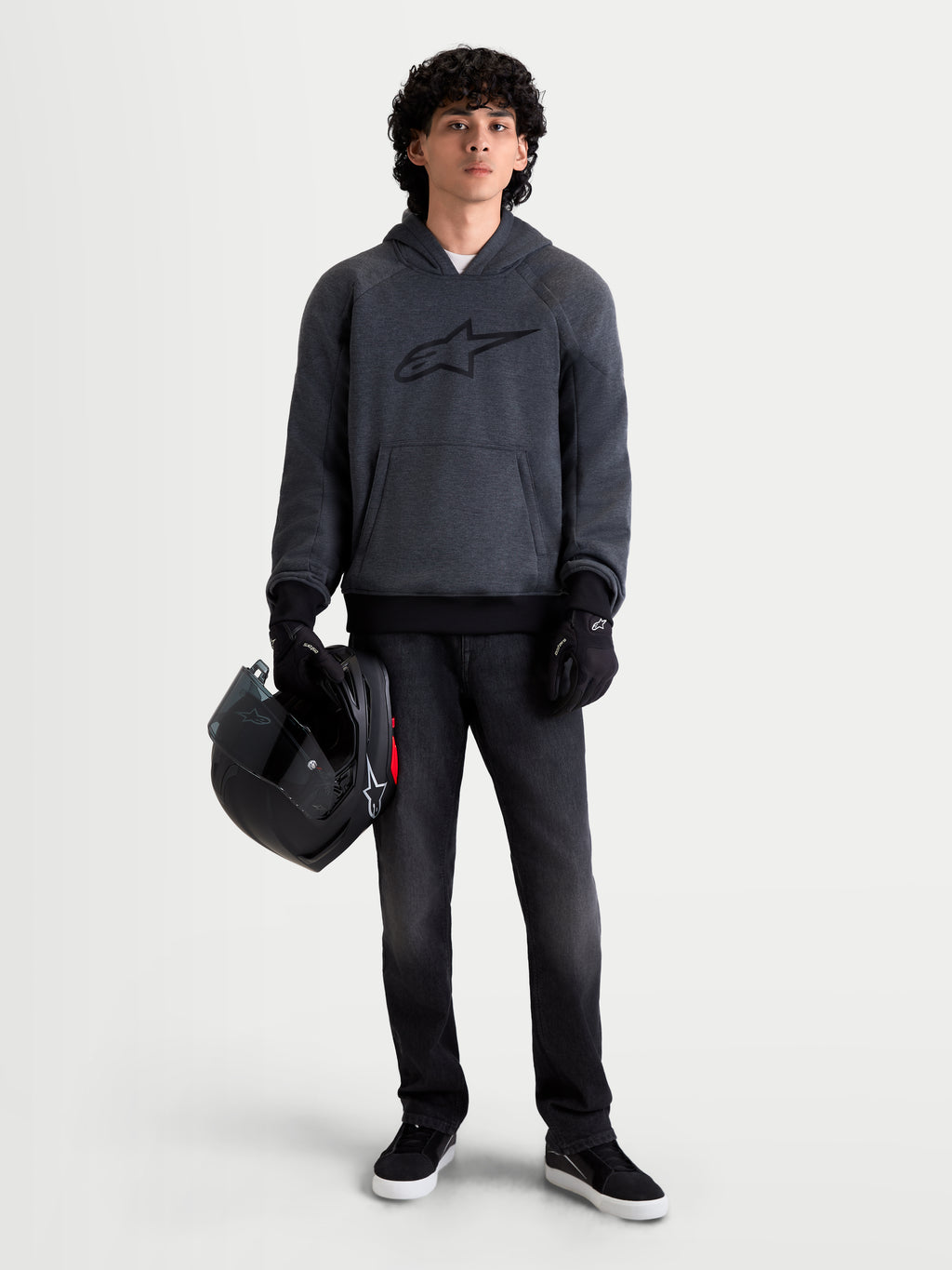 Alpinestars Ageless Hoodie, men's urban motorcycle hoodie in asphalt melange gray, front view on a model wearing black riding gloves and holding a helmet, featuring integrated shoulder and elbow protection.