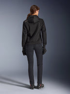 Alpinestars Stella Chrome Superairflow Hoodie, sweat à capuche technique de moto pour femme, maille 3D noire avec petit logo orange sur l'épaule, vue de dos, porté avec un pantalon de moto noir, des gants et des bottes noirs, conçu pour la conduite sportive urbaine