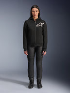 Femme portant le sweat à capuche Alpinestars Stella Chrome V2 Sport, noir avec logo Astars blanc sur la poitrine, associé à un pantalon de moto technique et des bottes noirs, design de vêtement de moto urbain.