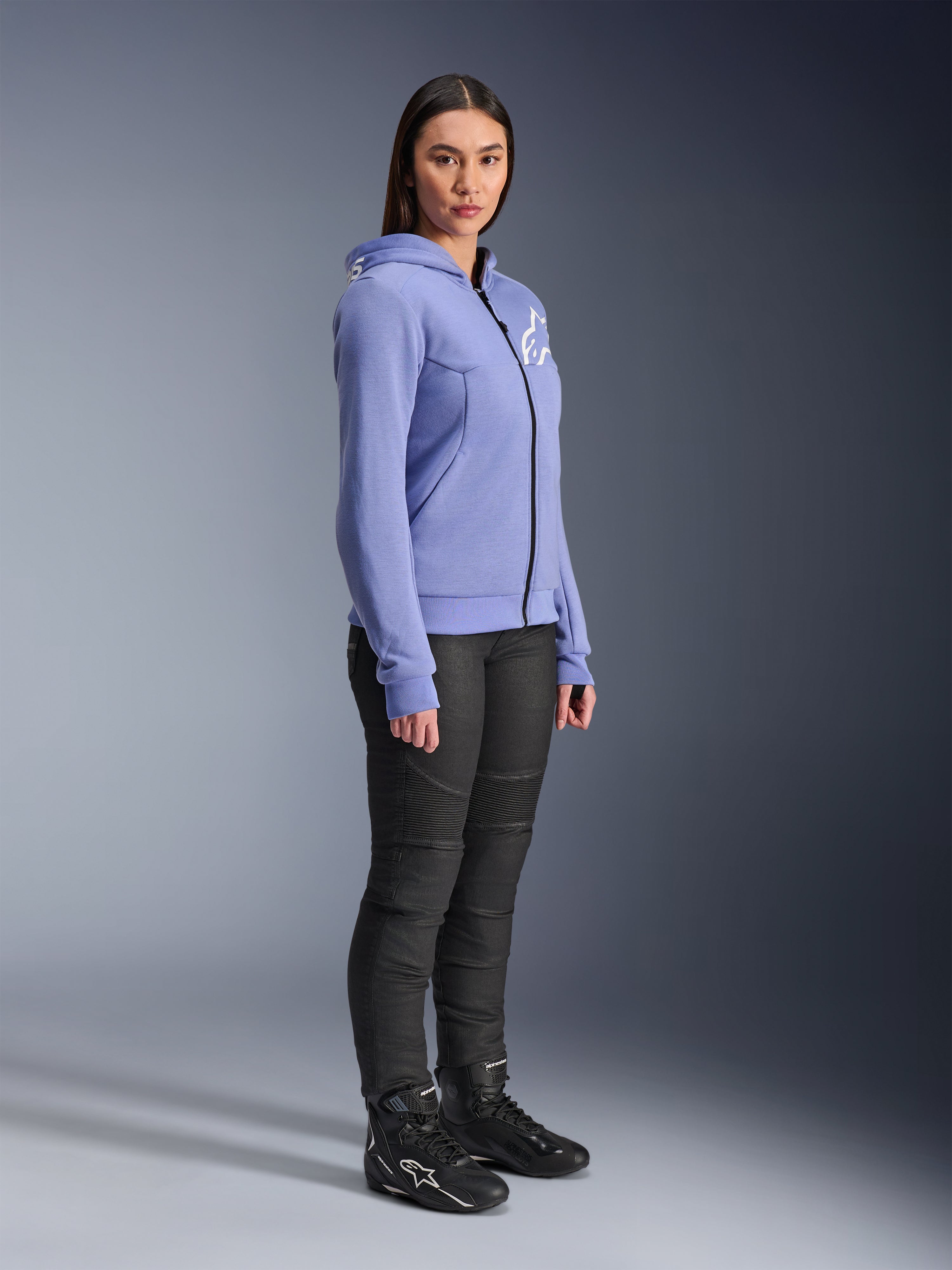 Alpinestars Stella Chrome V2 Sport Hoodie voor dames, motorhoodie in blauw-violet met wit Alpinestars-logo op de borst, model draagt zwarte motorbroek en zwarte motorlaarzen, stedelijke motorkleding voor dames