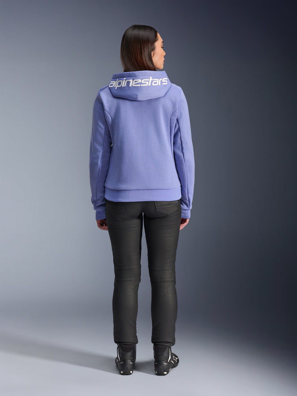 Alpinestars Stella Chrome V2 Sport Hoodie, Blue Violet, achteraanzicht van een vrouw die de hoodie draagt met wit Alpinestars-logo op de capuchon, gecombineerd met zwarte broek en motorlaarzen, casual stedelijke motorkleding