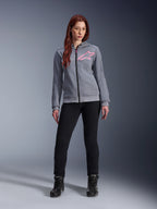 Alpinestars Stella Chrome V2 Sport Hoodie, Gray Heather Pink Fluo, gedragen door een vrouw met zwarte broek en laarzen, met een roze Alpinestars-sterlogo op de borst, urban motorkleding met volledige ritssluiting, lichtgewicht tech fleece met een casual atletische pasvorm.