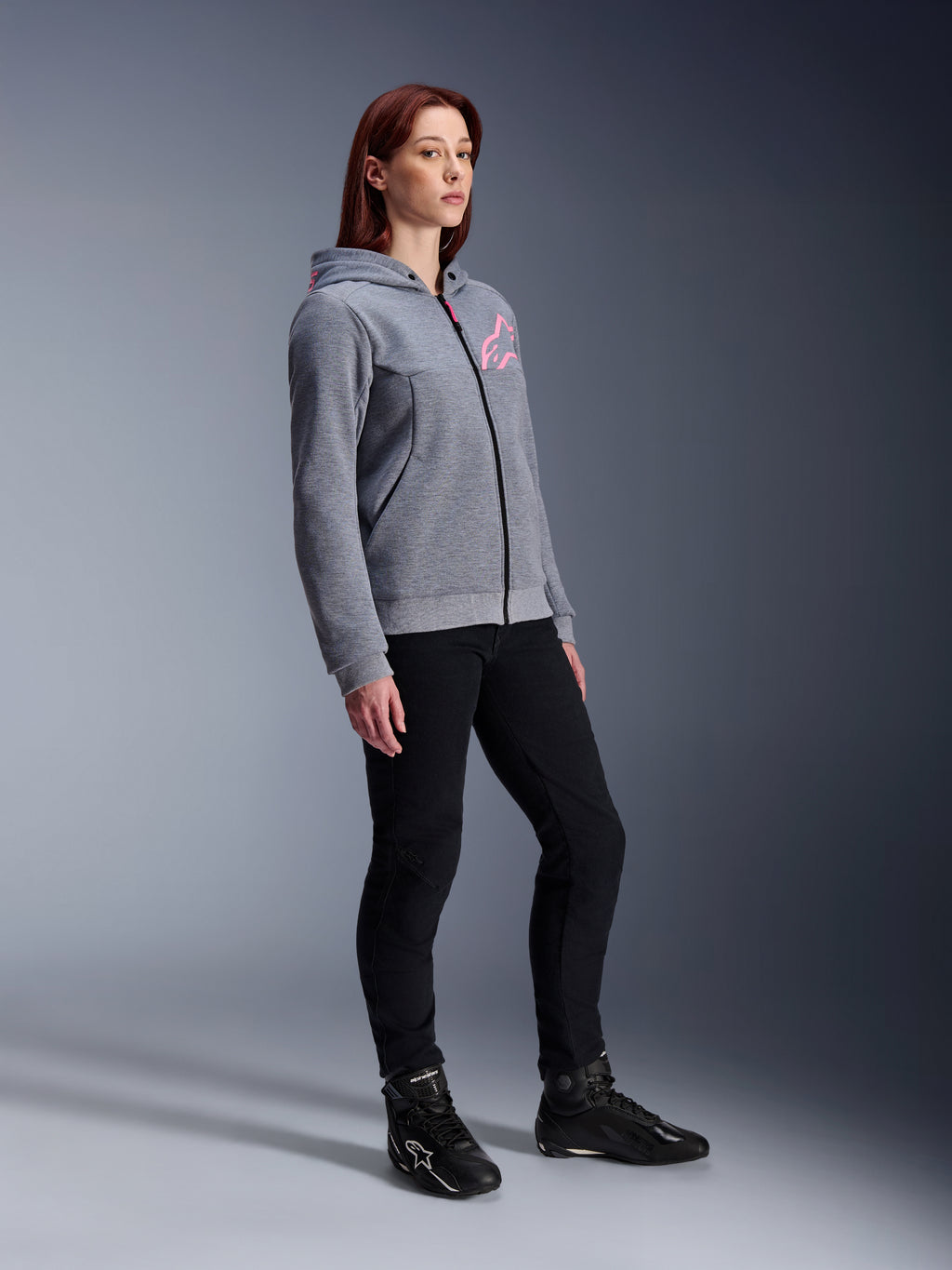 Alpinestars Stella Chrome V2 Sport Hoodie, motorhoodie voor dames, gemêleerd grijs en fluoroze, gedragen met een zwarte motorbroek en zwarte laarzen, casual urban motorkleding
