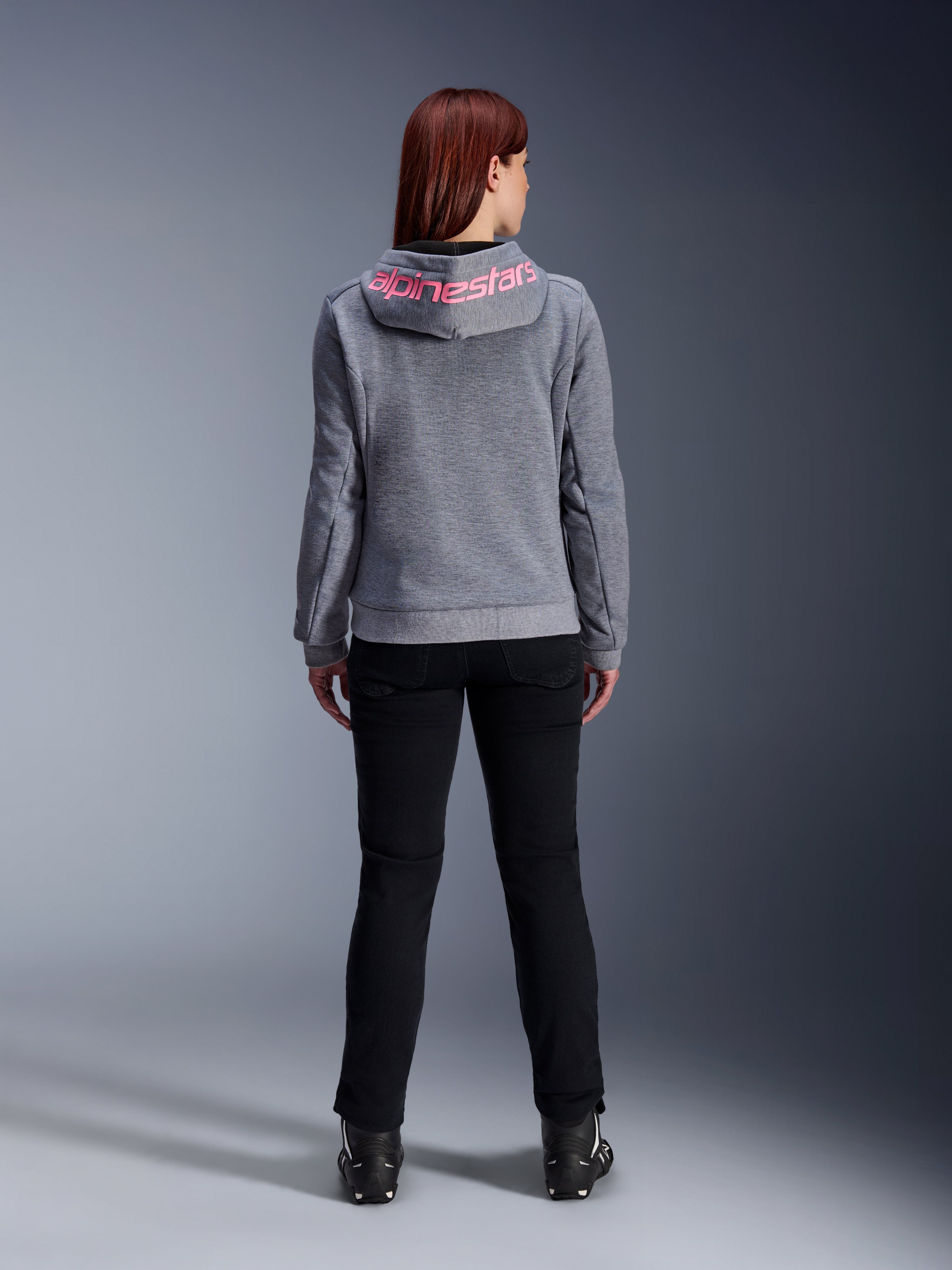 Alpinestars Stella Chrome V2 Sport Hoodie, motorhoodie voor dames, Gray Heather en Pink Fluo, achteraanzicht met roze Alpinestars-logo op de capuchon, gedragen met een zwarte motorbroek en laarzen, casual motorkleding voor dames