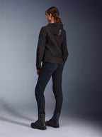 Alpinestars Stella Radium Tech Hoodie, zwarte urban motorhoodie voor dames, achteraanzicht met 'ALPIN'-branding op de capuchon, gecombineerd met een zwarte technische motorbroek en zwarte laarzen, lichtgewicht windbestendige tech shell.