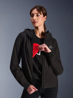 Alpinestars Stella Radium Tech Hoodie voor dames, zwarte urban motorhoodie, vrouwelijk model toont de rode Nucleon Flex Plus-bescherming aan de binnenkant, lichtgewicht 3-laags winddichte textiele buitenlaag met geribde manchetten en logopatch op de borst, beschermende motorkleding