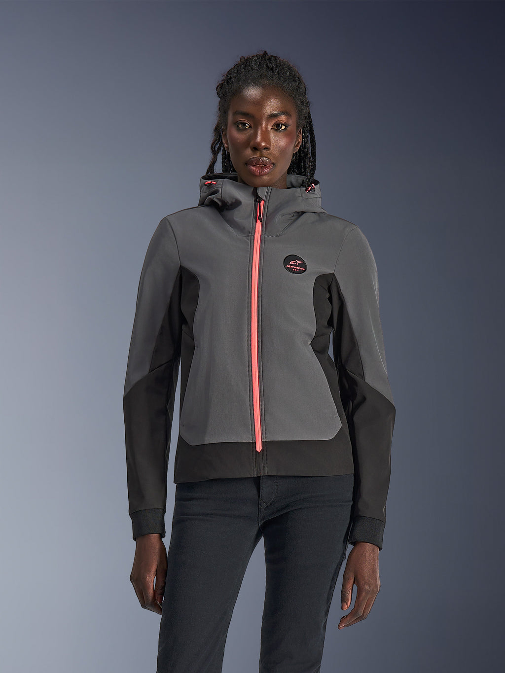 Alpinestars Stella Radium Tech Hoodie, veste à capuche de moto pour femme, gris foncé et noir avec fermeture éclair et cordons de serrage rose vif, porté par un mannequin, design urbain sportif avec logo Alpinestars sur la poitrine