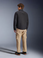 Surchemise Alpinestars Bryon WR, noire, vue de dos sur mannequin, associée à un pantalon cargo beige et des baskets noires, veste de moto urbaine avec texture en toile cirée et design arrière épuré et minimaliste