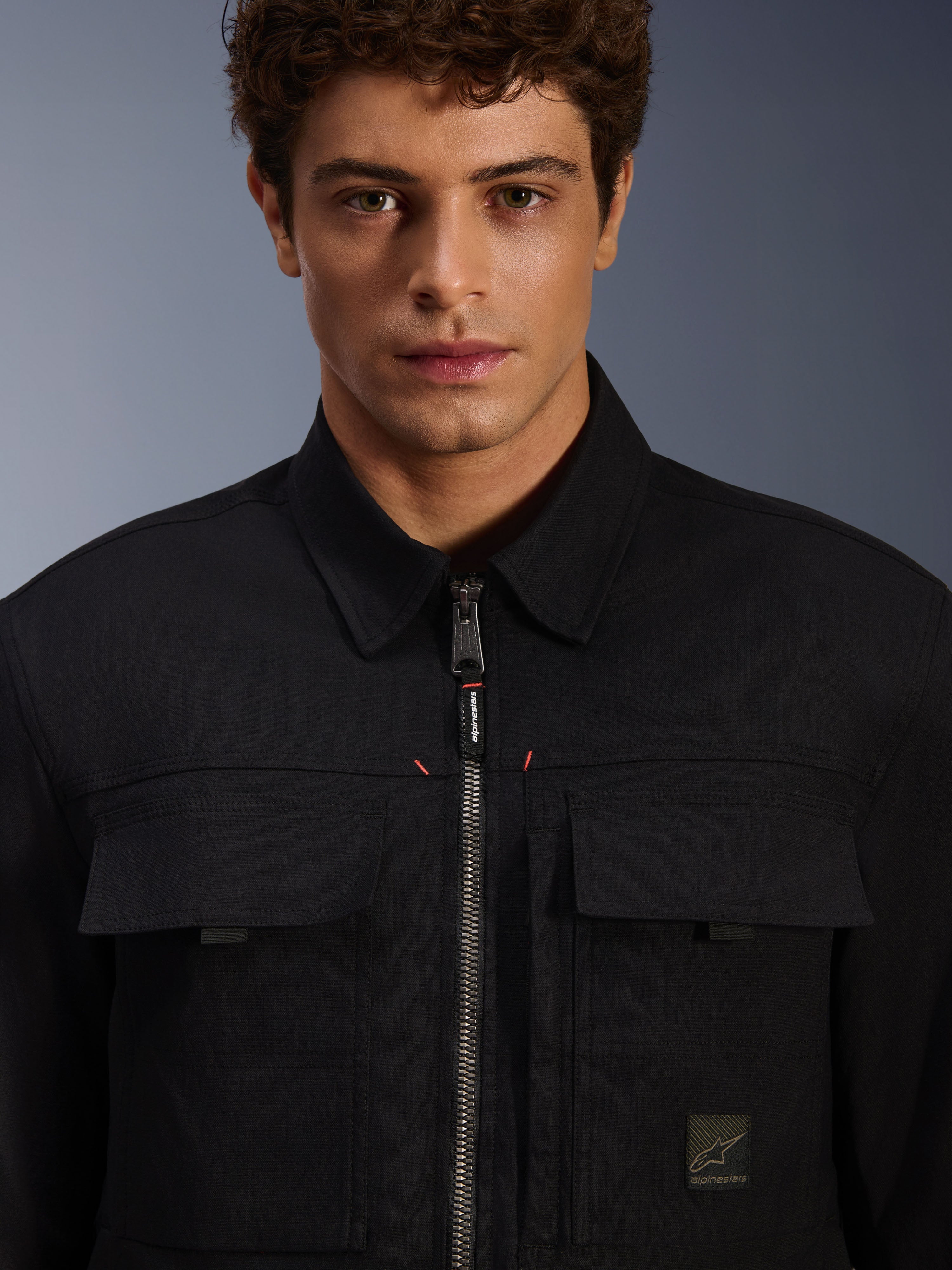 Alpinestars Bryon Water Resistant Overshirt, noire, vue rapprochée de la fermeture éclair frontale et des poches de poitrine, texture en toile cirée durable, design urbain minimaliste avec finitions de la marque et étiquette logo tissée