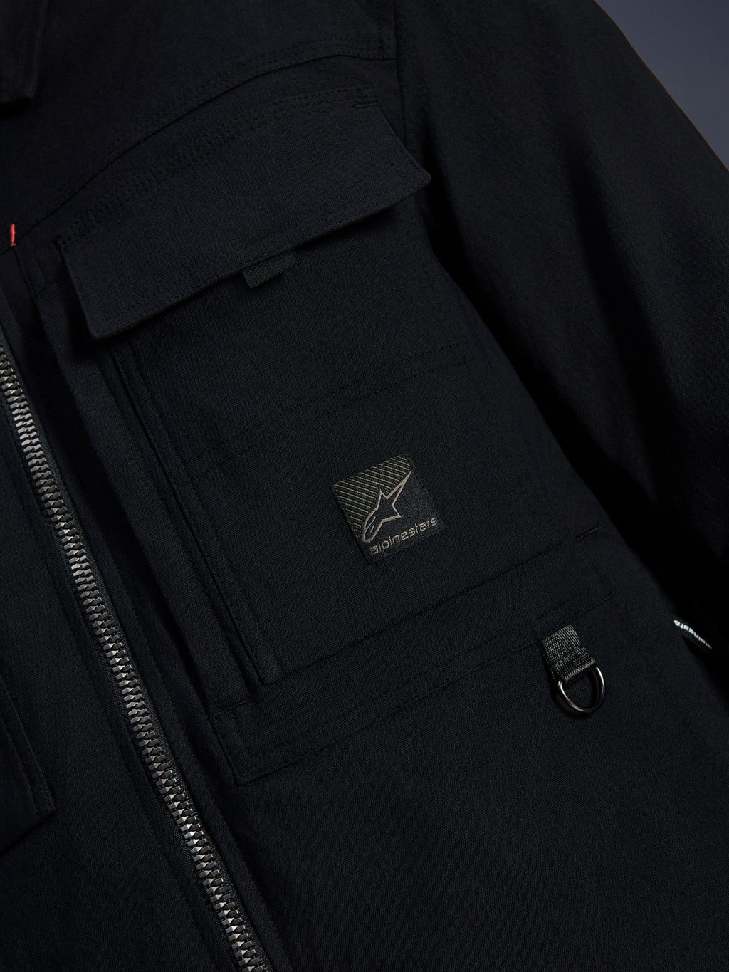 Surchemise Alpinestars Bryon Water Resistant, noir, vue rapprochée du tissu en toile cirée, fermeture éclair avant, poche cargo sur la poitrine avec écusson du logo Alpinestars et détail d'anneau en D en métal