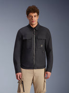 Surchemise Alpinestars Bryon Water Resistant, noire, veste de moto urbaine au style workwear, avec deux grandes poches cargo sur la poitrine et une fermeture éclair intégrale, fabriquée en toile cirée, portée par un mannequin avec un pantalon cargo beige pour un look utilitaire contemporain.