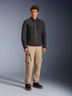 Surchemise résistante à l'eau Alpinestars Bryon, noir, portée par un mannequin homme avec un pantalon cargo kaki et des chaussures noires, veste de moto urbaine au design inspiré du vêtement de travail, photo de studio en pied