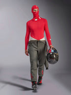 Alpinestars ZX Evo V3 bivakmuts in het rood, gedragen door een autocoureur met een bijpassende rode basislaag met lange mouwen en een grijze racebroek, houdt een koolstofvezel helm vast, professionele vlamvertragende autosportuitrusting
