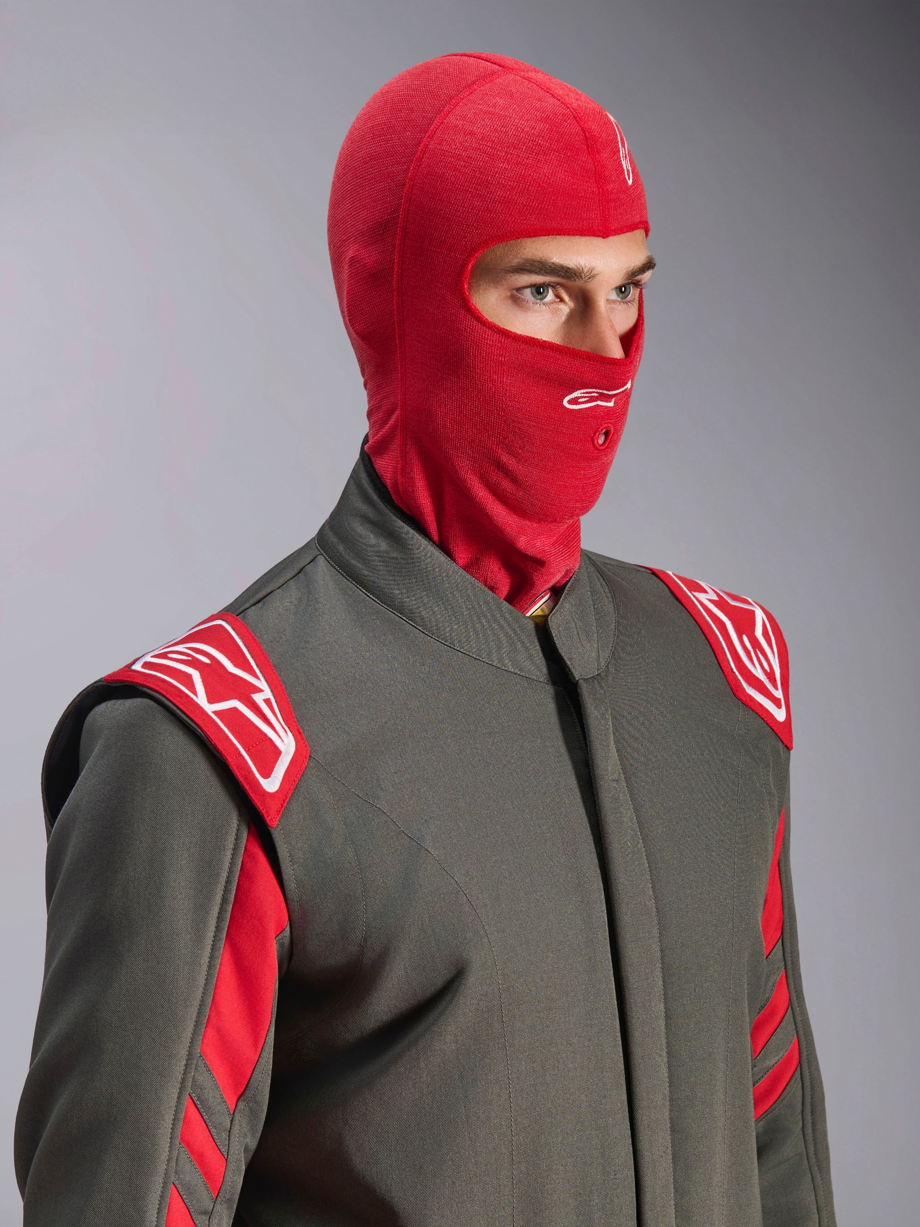 Alpinestars ZX Evo V3 bivakmuts, rood, gedragen door een coureur in een grijs racepak met rode en witte accenten, met een wit Astars-logo op het voorhoofd en een opening voor een hydratatiebuis, vlamvertragende onderlaag voor autoraces