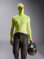 Alpinestars ZX Evo V3 bivakmuts, basislaag voor autoraces, Yellow Fluo, gedragen met bijpassende top met lange mouwen en racebroek, model houdt een helm van koolstofvezel met iriserend vizier vast, professionele vlambestendige motorsportuitrusting