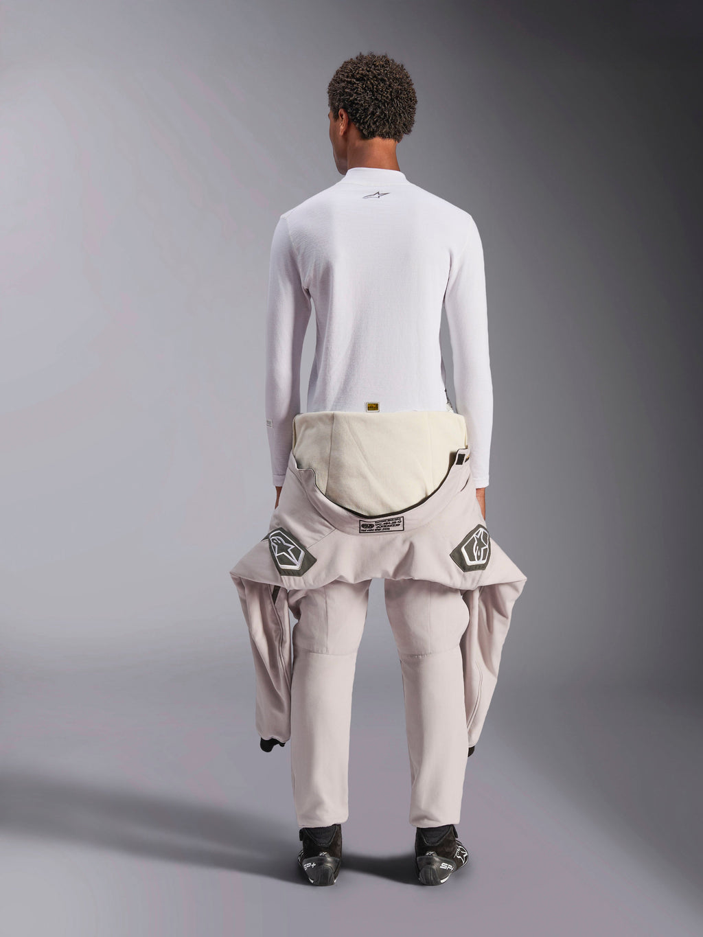 Alpinestars ZX Evo V3 Top - Lange Mouwen, witte auto racing baselayer, achteraanzicht van een persoon die de vlamwerende top draagt met een racepak tot aan de taille naar beneden gerold, gecombineerd met zwarte racelaarzen, professioneel motorsportondergoed