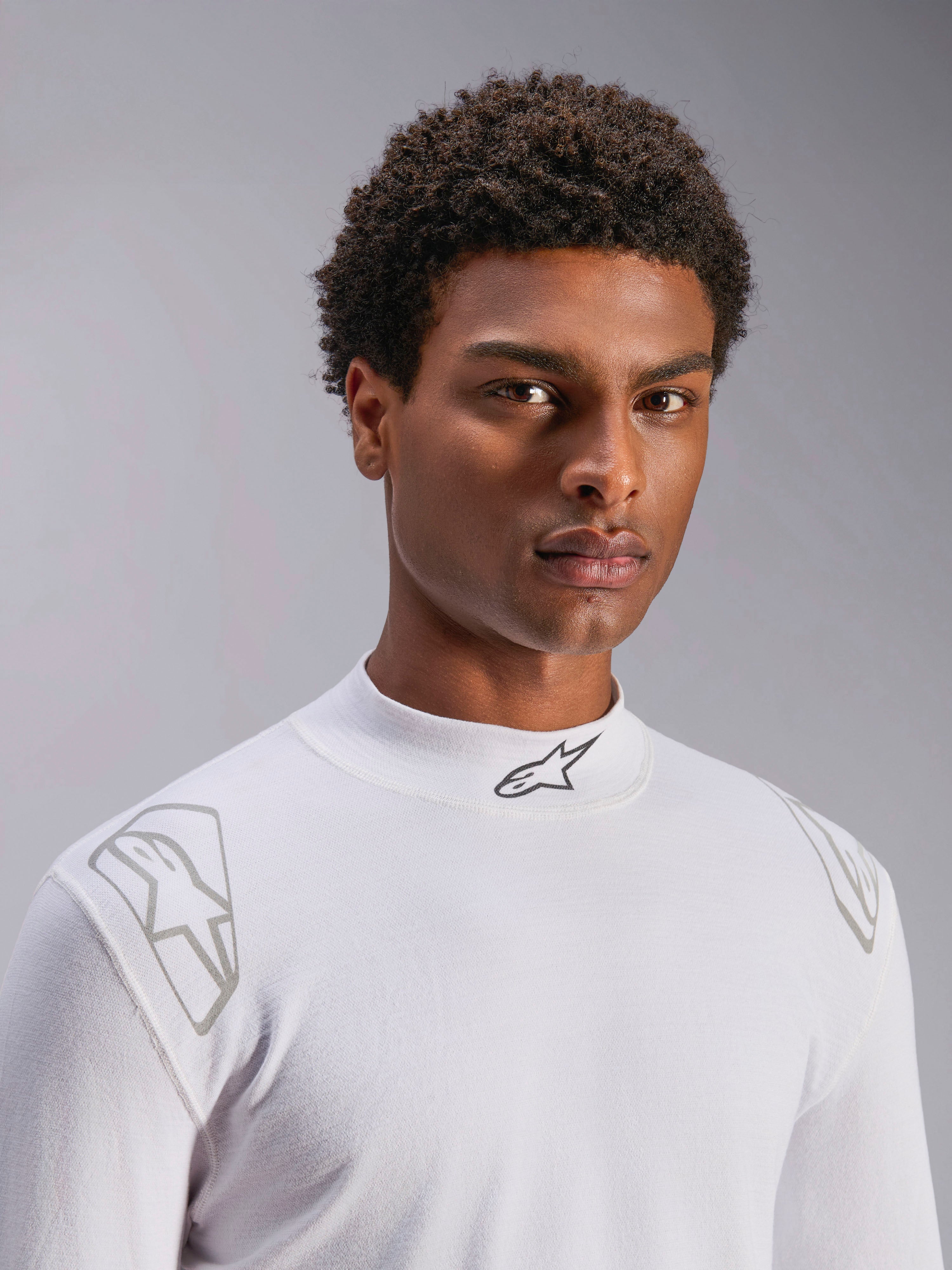Alpinestars ZX Evo V3 Top - Lange mouwen, witte autorace baselayer, gedragen door een mannelijk model, opstaande kraag met zwart Alpinestars-logo, zilveren grafische prints op de schouders, lichtgewicht vlamvertragend autosportondergoed
