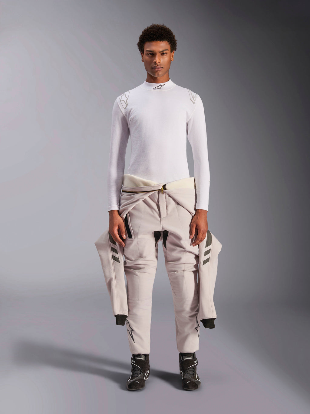 Alpinestars ZX Evo V3 Top, lange mouwen, wit, auto racing baselayer gedragen met een lichtgekleurd racepak om de taille geknoopt en zwarte raceschoenen, voorzien van een opstaande kraag met logo en branding op de schouders, professioneel vlamvertragend motorsportondergoed