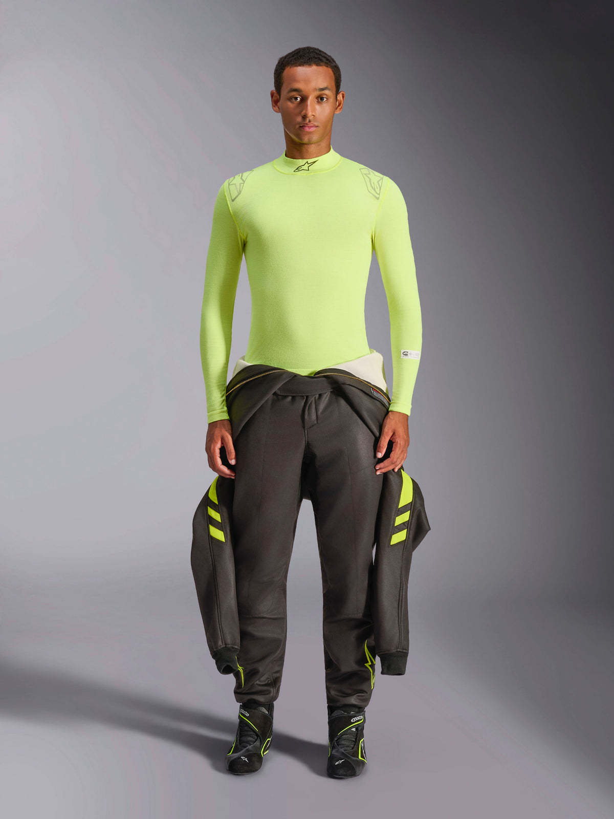 Alpinestars ZX Evo V3 Top - Lange Mouwen, Geel Fluo, gedragen door een model met een donkere racebroek en laarzen, met een mock neck en atletische pasvorm, vuurbestendige basislaag voor professionele autosport