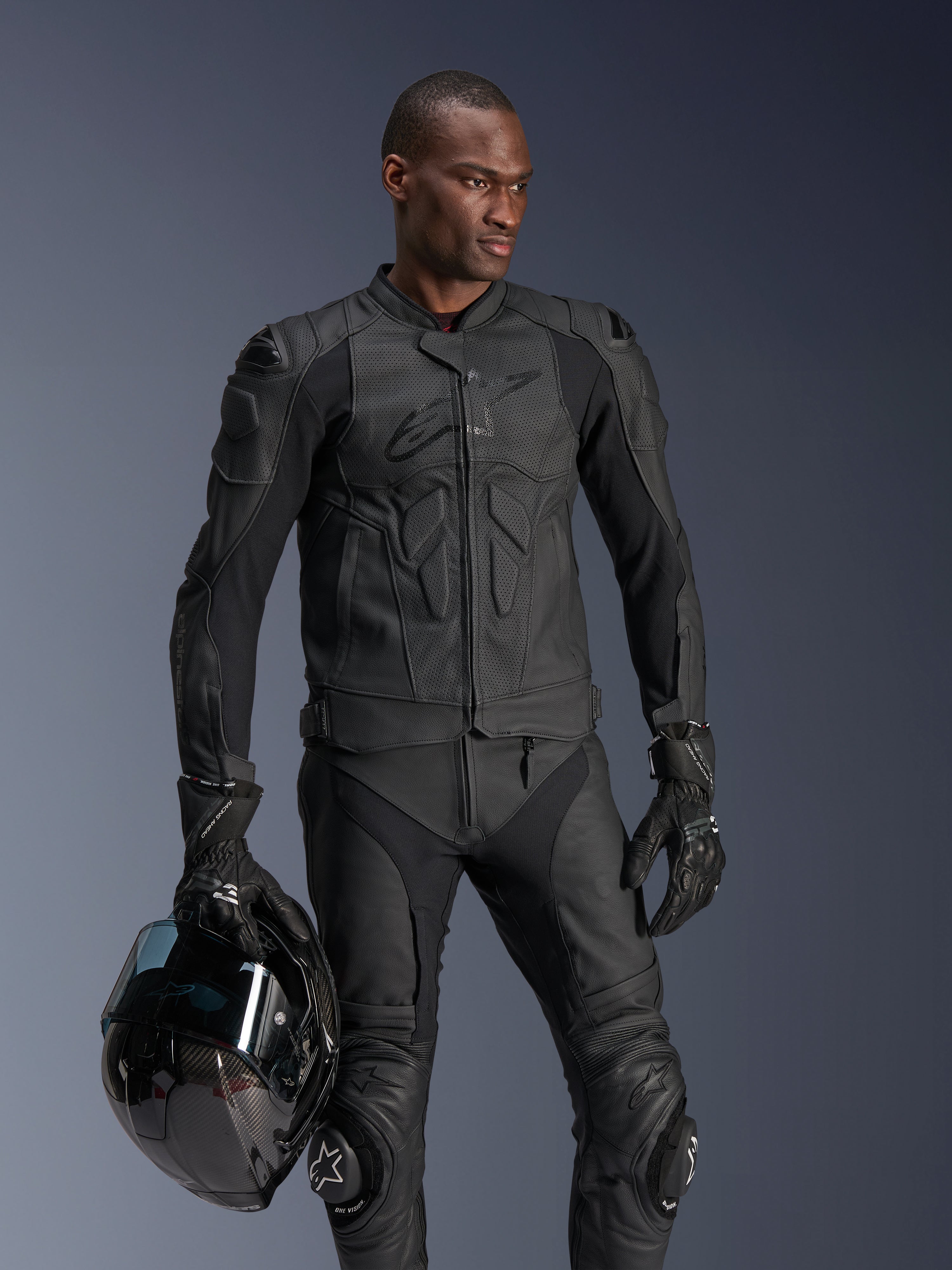 Alpinestars Dusk Airflow Leren Jas, zwart, gedragen door een mannelijke rijder met bijpassende leren broek en handschoenen, houdt een zwarte helm vast, voorzien van geperforeerde leren panelen en geïntegreerde bescherming voor sportief motorrijden