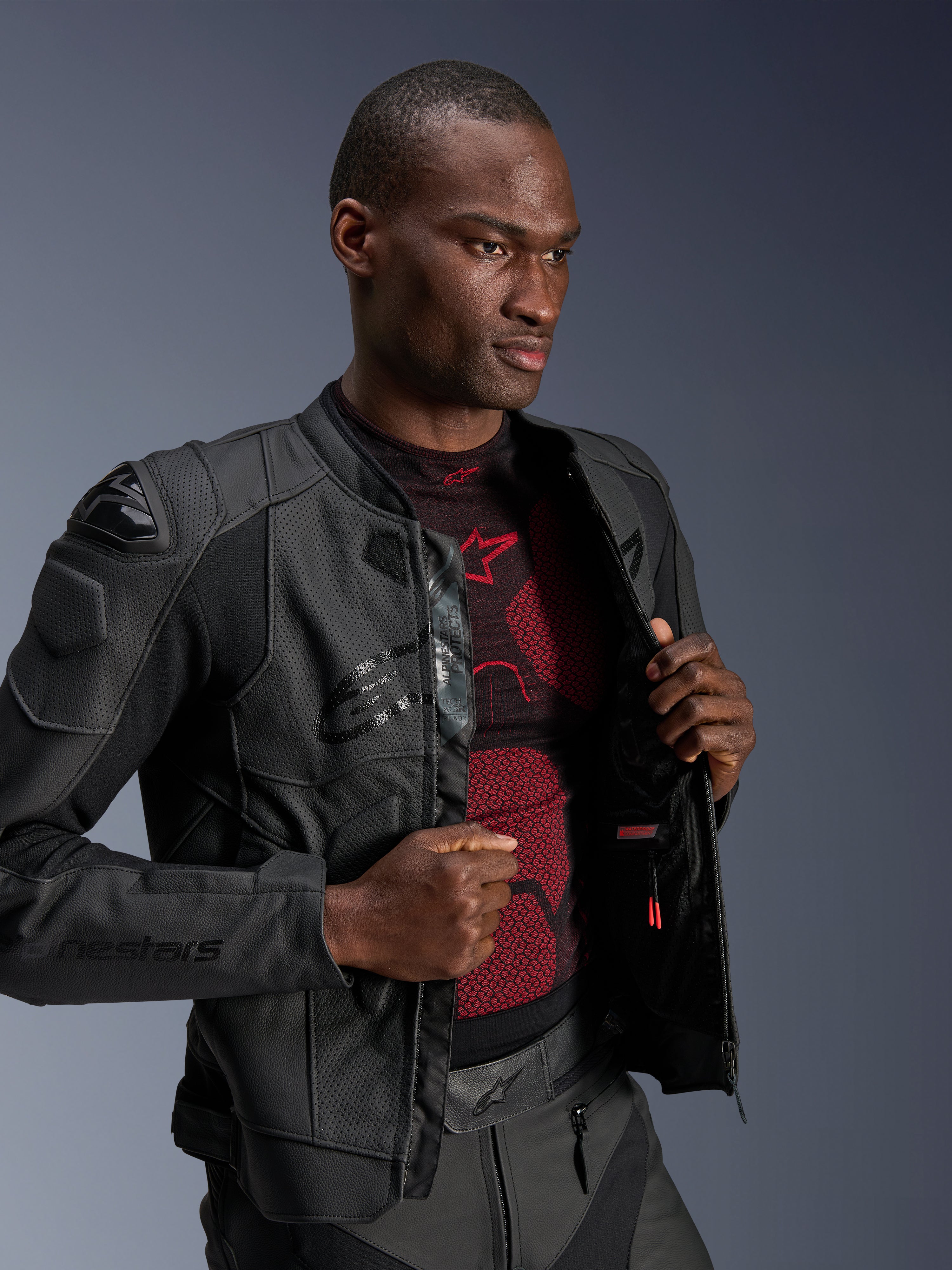 Alpinestars Dusk Airflow Leren Jas, Black Black, gedragen door een mannelijk model over een rood-zwarte basislaag, voorzien van geperforeerde leren panelen, externe DFS schoudersliders en een sportieve pasvorm.