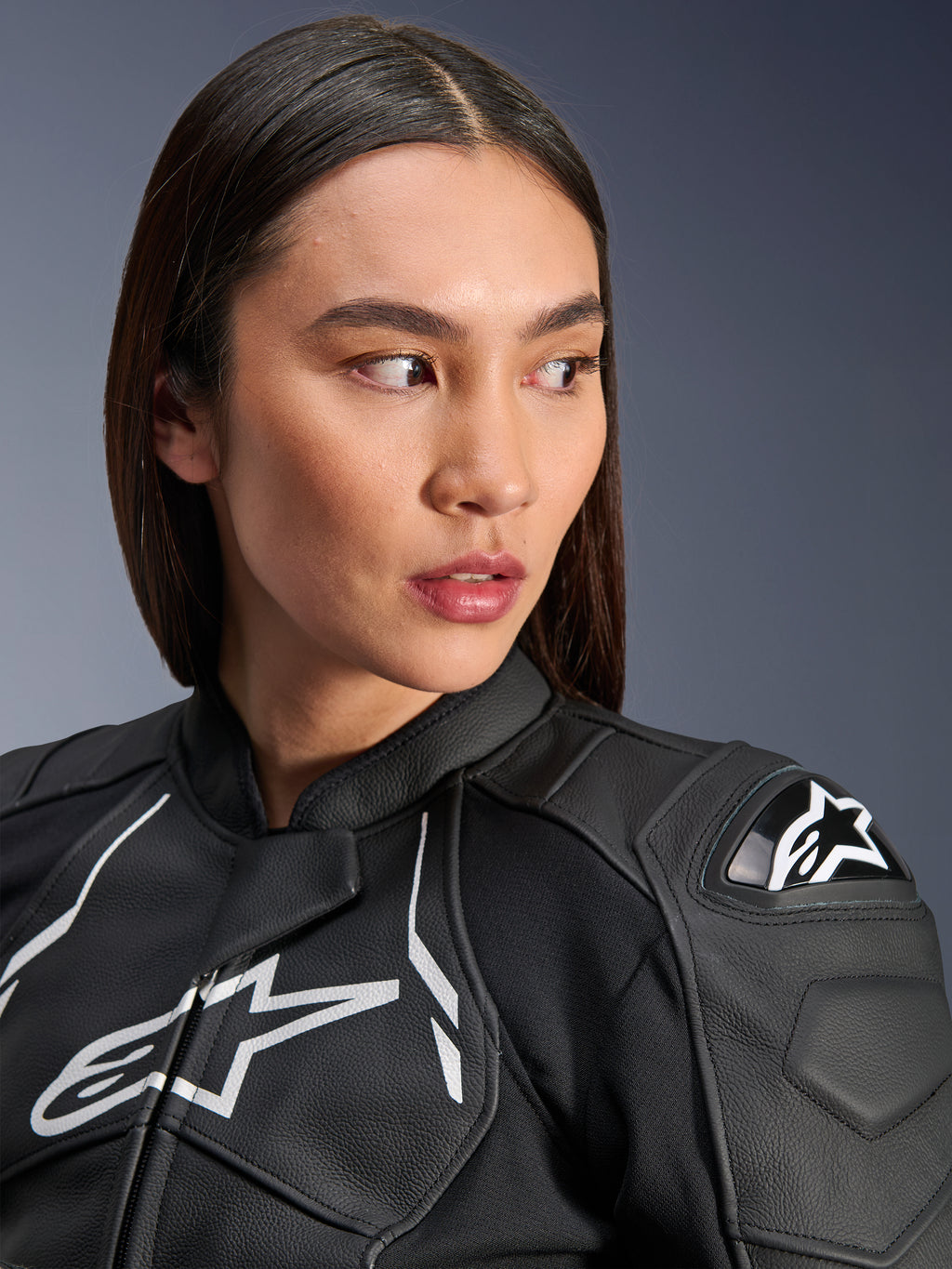 Vrouw die de Alpinestars Stella Dusk Leren Jas in zwart en wit draagt, close-up portret met het witte Alpinestars-logo op de borst en externe DFS-schouderbeschermer, hoogwaardige lederen constructie voor motorwegracen