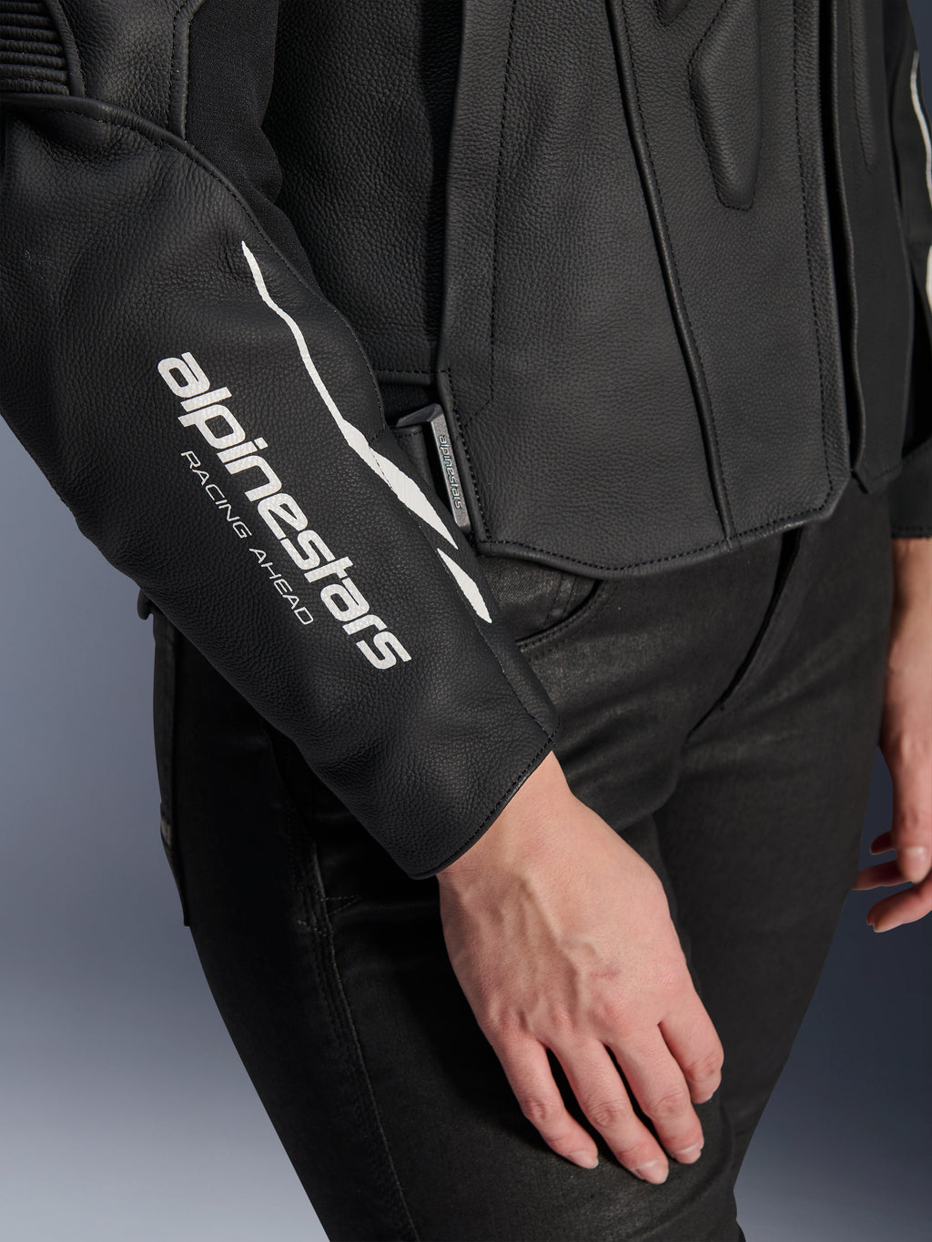 Alpinestars Stella Dusk leren jas, zwarte leren motorjas voor dames, close-up met wit 'alpinestars RACING AHEAD' logo op de mouw, premium runderleer textuur, gedragen met zwarte broek