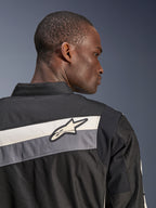 Veste Alpinestars T-Dyno WR, veste de moto en textile, noir, gris foncé et écru, gros plan du haut du dos et de l'épaule avec bandes horizontales et logo étoile Alpinestars, portée par un mannequin, design d'inspiration vintage pour la route