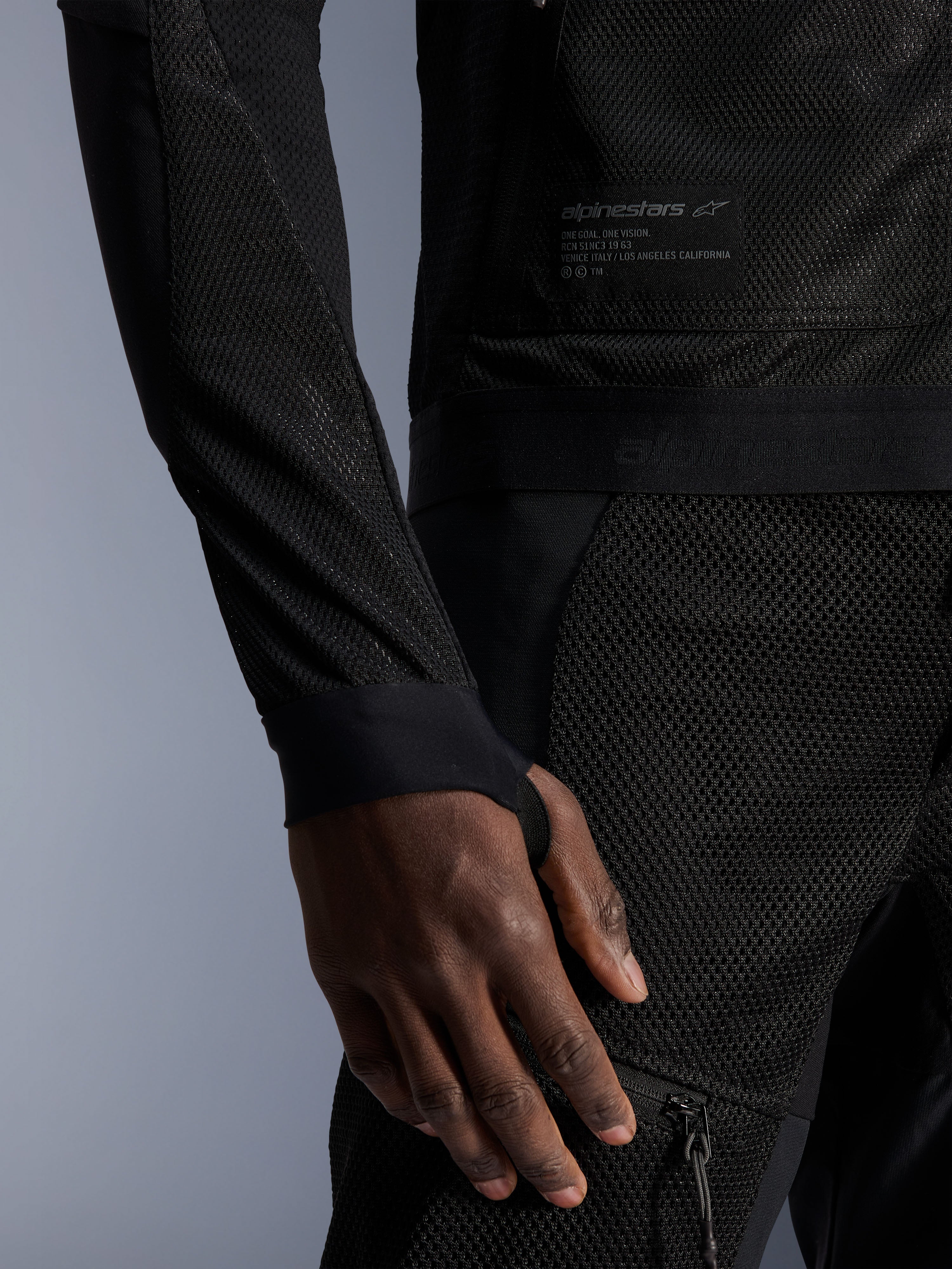 Alpinestars Troop-Air jas, zwart, close-up van de technische mesh-constructie, merkpatch met technische tekst en mouw met geïntegreerde duimgatlus, urban zomer motorjas met high-airflow ontwerp