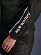 Alpinestars Stella T-SPS Air V2 Jacket, Women's Motorcycle Jacket, Black and White, close-up of the sleeve featuring white Alpinestars logo and T-SPS AIR text, mesh and textile construction for airflow, worn with black riding pants