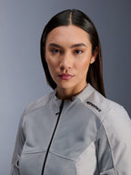 Veste Alpinestars Stella C-1 Air, veste de moto argentée pour femme, portrait rapproché montrant les panneaux de ventilation en maille technique et le logo noir sur l'épaule, équipement de conduite urbain contemporain