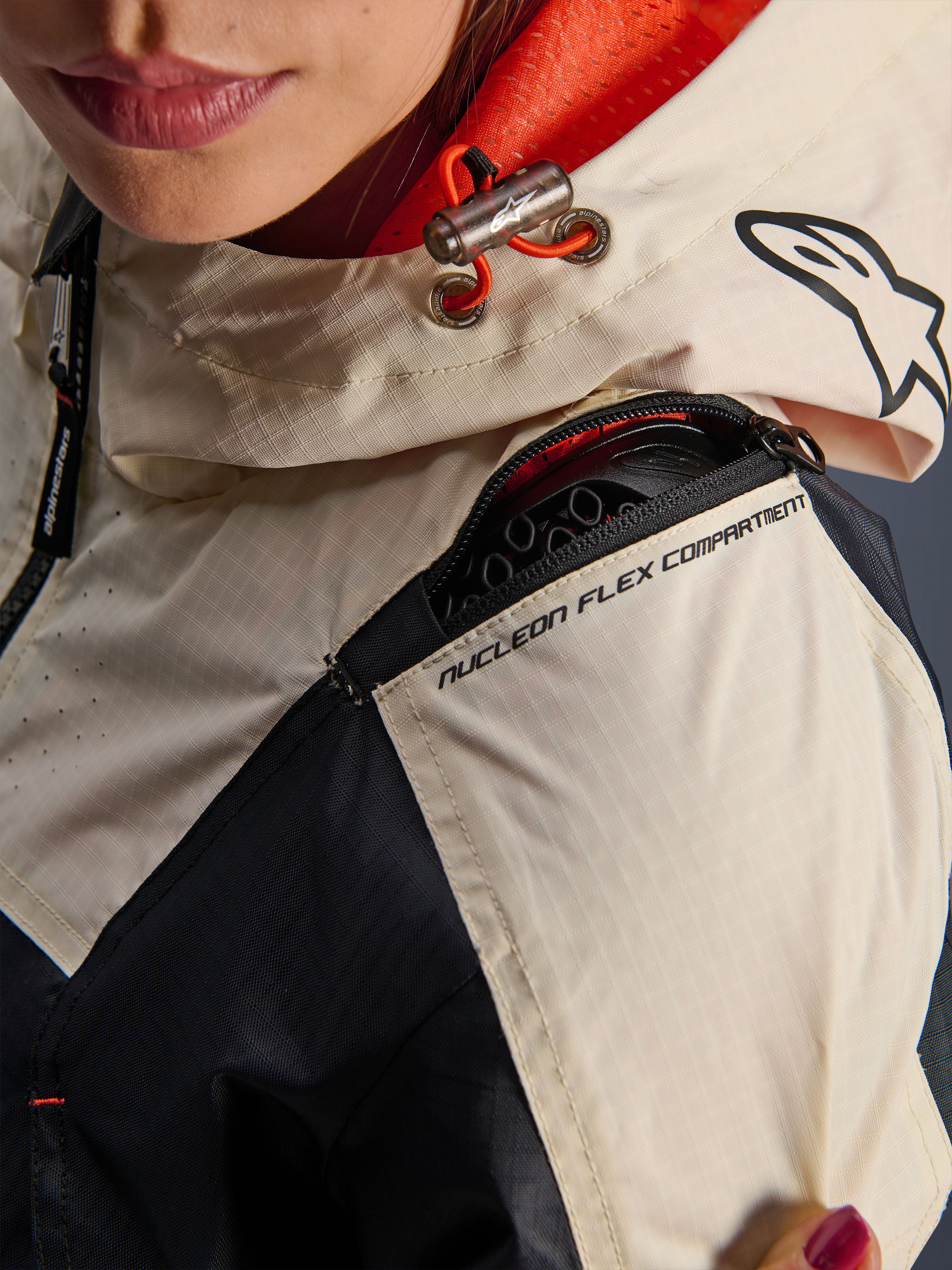 Alpinestars Molly Air jas, motorjas voor dames, Black Almond, detailopname van de schouder met de rits van het Nucleon Flex-compartiment, ripstop-stof en oranje mesh-voering in de capuchon
