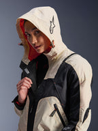 Alpinestars Molly Air Jacket in Black Almond, gedragen door een vrouwelijk model met de capuchon op, met crème en zwarte kleurvlakken, een opvallende oranje mesh voering en technische urban designelementen waaronder een sterlogo en ritsdetails.