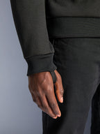 Alpinestars Chrome V2 Sport Hoodie, polaire technique noire, gros plan sur le poignet de manche côtelé avec passe-pouce intégré pour la stabilité lors de la conduite, détail de vêtement de moto urbain