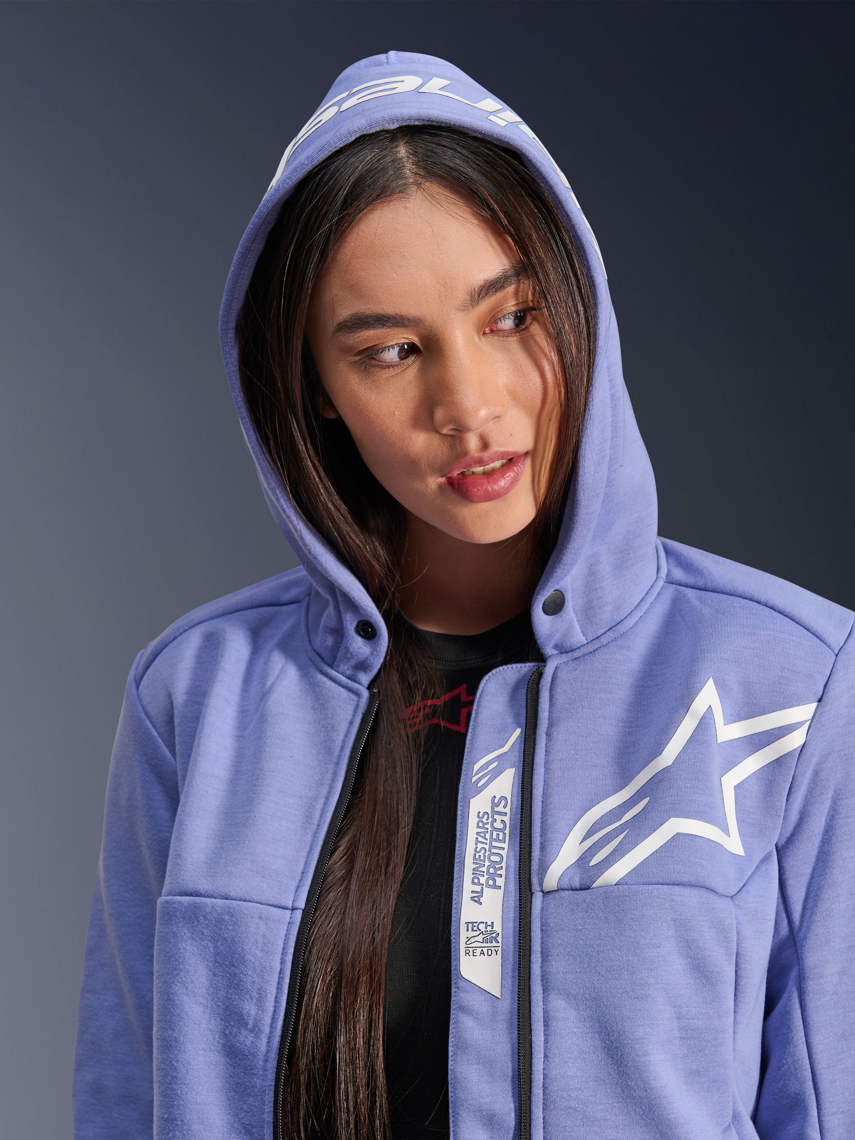 Alpinestars Stella Chrome V2 Sport Hoodie, motorhoodie voor dames, blauw-violet met wit sterlogo, voorzien van 'Alpinestars Protects' en 'Tech-Air Ready' branding langs de rits, casual stedelijk ontwerp met de capuchon omhoog.