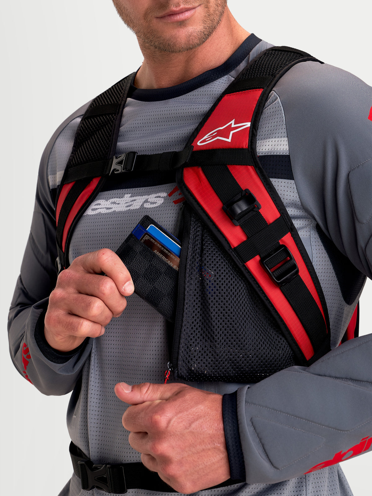 Alpinestars AT-9 Rucksack, Motocross-Rucksack, Schwarz und Leuchtrot, Nahaufnahme mit gepolstertem Schultergurtsystem und Reißverschluss-Netzzubehörtasche am Model