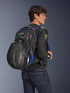 Alpinestars FQ20 City Hunter V2 Monster rugzak, stedelijke motorrugzak, zwart met fluo rode, blauwe en groene accenten, model draagt een zwarte helm in de mesh-houder aan de achterzijde, gestyled met een zwarte motorjas en blauwe jeans.