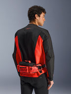 Alpinestars MM93 Waist Bag, motorheuptas, felrood en zwart, gedragen over een bijpassende zwart-rode motorjas, met ritsvakken en Marc Marquez MM93-branding, duurzame textielconstructie voor motorrijden