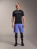 Alpinestars A-Aria Lite Short en Baja Blue, short de VTT pour homme, porté avec un maillot noir à manches courtes et des genouillères de protection, doté de perforations laser pour la ventilation, équipement de performance pour VTT