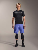 Maillot Alpinestars A-Aria Switch, maillot de VTT à manches courtes, noir avec logo Alpinestars blanc en miroir, porté par un mannequin homme avec un short de cyclisme bleu et des genouillères noires, vêtement de performance respirant pour le trail