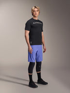 Mannequin homme portant des vêtements de VTT Alpinestars, incluant le maillot A-Aria Switch SS noir et le short A-Aria Lite bleu Baja, avec des genouillères noires, des chaussettes noires et des chaussures de VTT noires, photo de studio en pied.