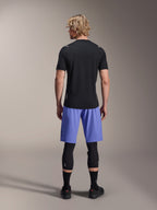 Cycliste homme portant le short Alpinestars A-Aria Lite, short de VTT, Baja Blue, vue de dos, avec maillot noir à manches courtes, genouillères noires et chaussures de cyclisme noires, équipement de VTT haute performance