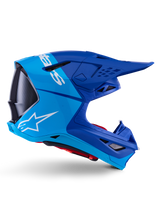 Alpinestars Supertech M10 Flood helm, motocrosshelm, metallic en medium blauw met zwarte carbon accenten, zijaanzicht, voorzien van een wit logo, aerodynamisch ontwerp met ventilatieopeningen, carbon fiber textuurdetails, professionele off-road racebescherming