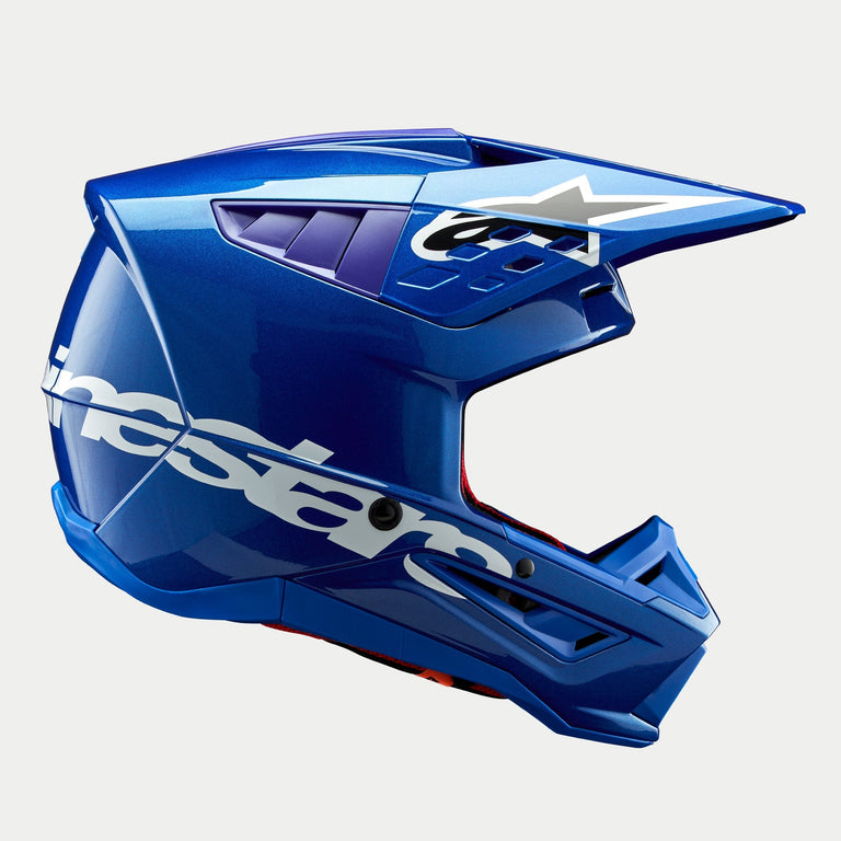 Alpinestars S-M5 Corp Helm ECE, glanzend blauwe motorcrosshelm, zijprofiel, opvallende witte Alpinestars-branding op de zijkant, paarse accenten in de ventilatieopeningen, lichtgewicht aerodynamische schaal voor off-road prestaties