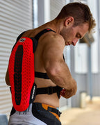 Alpinestars A-5 Plasma borstbeschermer, rood en zwart, met een getextureerde rugbeschermer met Nucleon PLASMA-technologie, gedragen door een man die zwarte bandjes verstelt, zijaanzicht dat de beschermende schaal en het flexibele ontwerp voor off-road rijden benadrukt