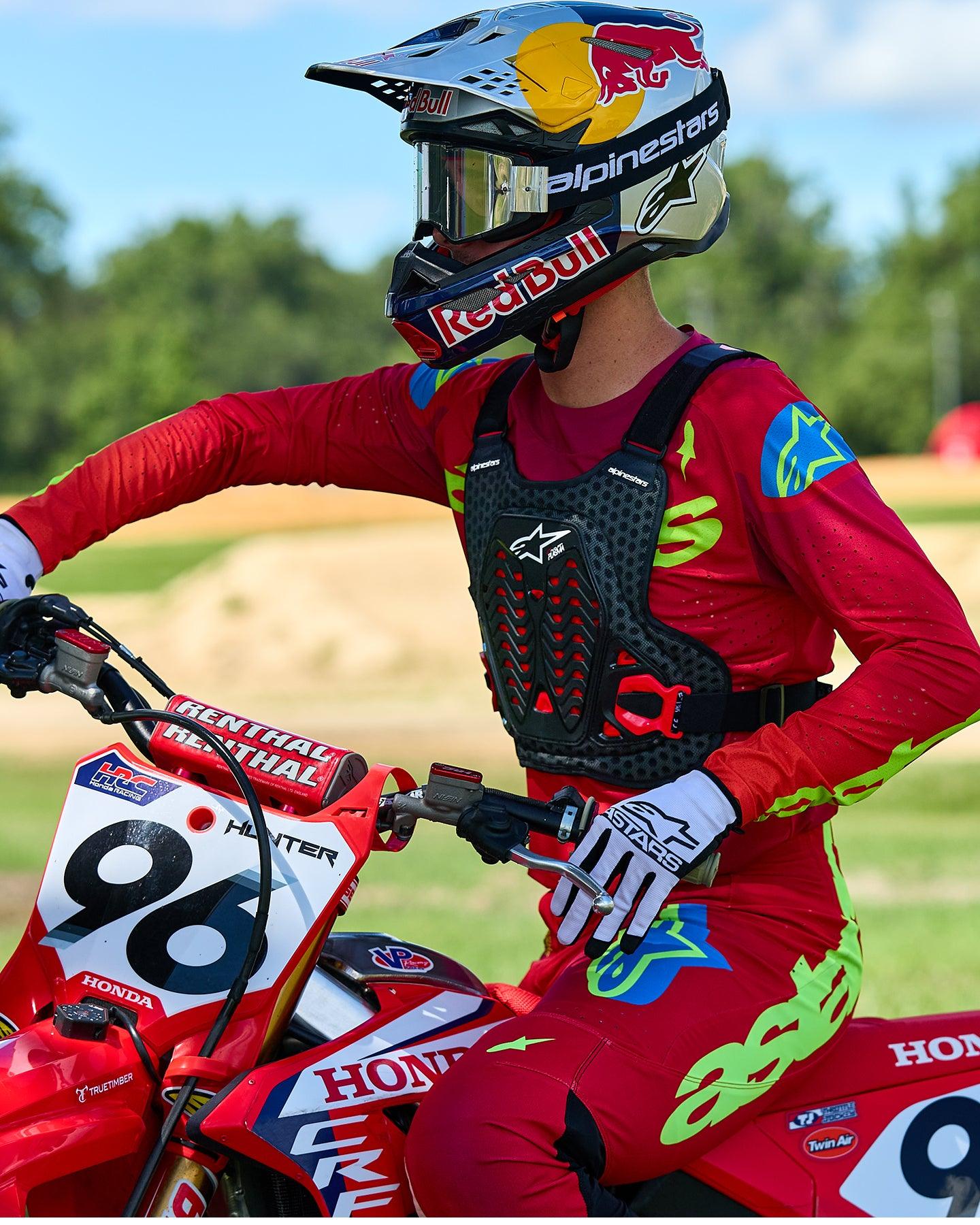 Motorcrossrijder met Alpinestars A-5 Plasma borstbeschermer in zwart en rood, gecombineerd met een rood en limegroen racejersey en broek, zittend op een rode Honda motorfiets, hoogwaardige off-road beschermende uitrusting