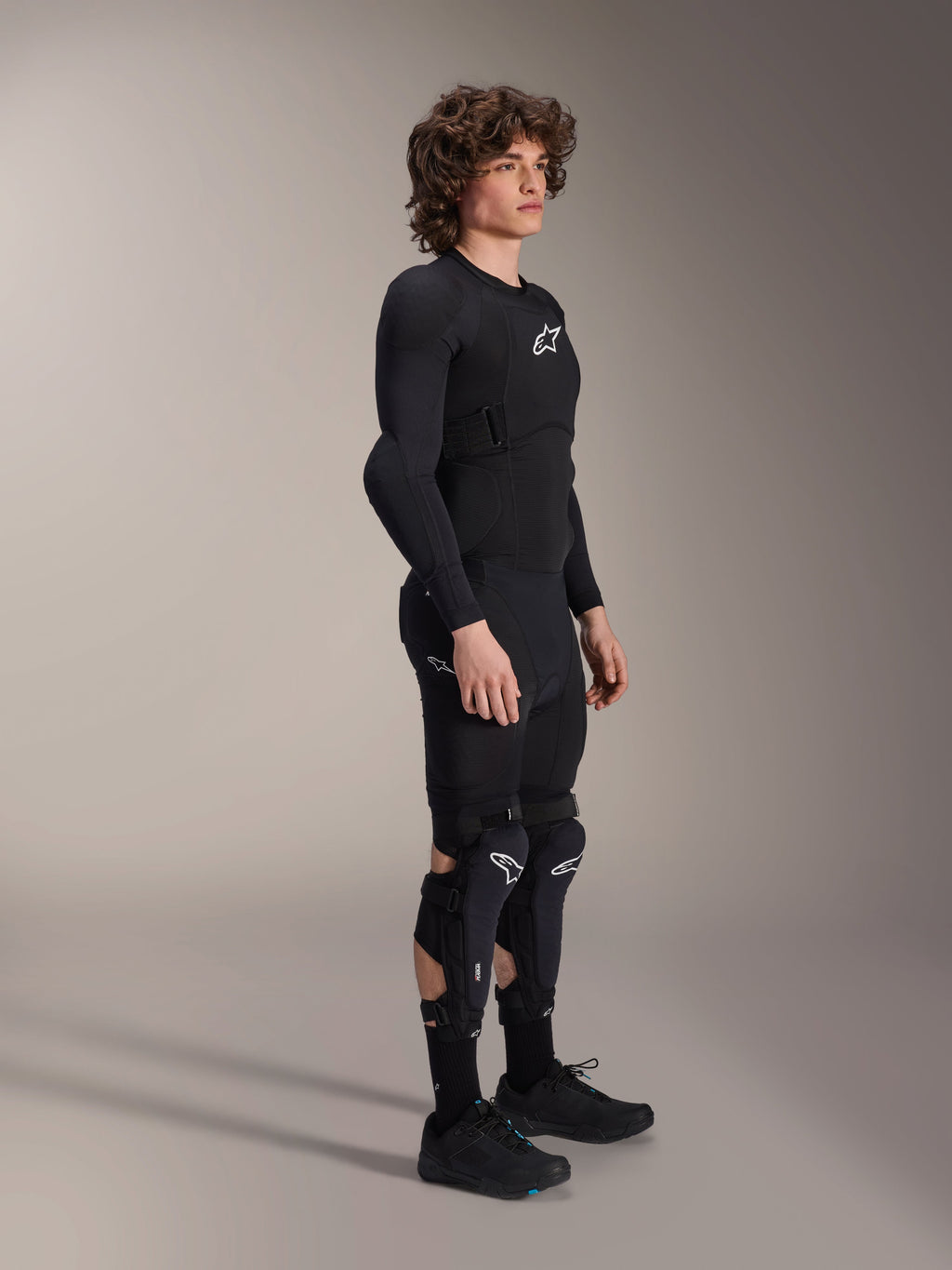 Veste de protection Alpinestars A-Impact Plasma - Manches Longues, noire, portée par un mannequin avec un équipement de protection assorti incluant genouillères et short, logos Astars blancs, conception en mesh respirant et design profilé pour le cyclisme tout-terrain.