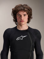 Modèle masculin portant une veste de protection Alpinestars A-Impact Plasma à manches longues, noire avec logo Astars blanc, dotée d'une fermeture éclair frontale décalée et d'un rembourrage intégré, équipement de protection VTT professionnel